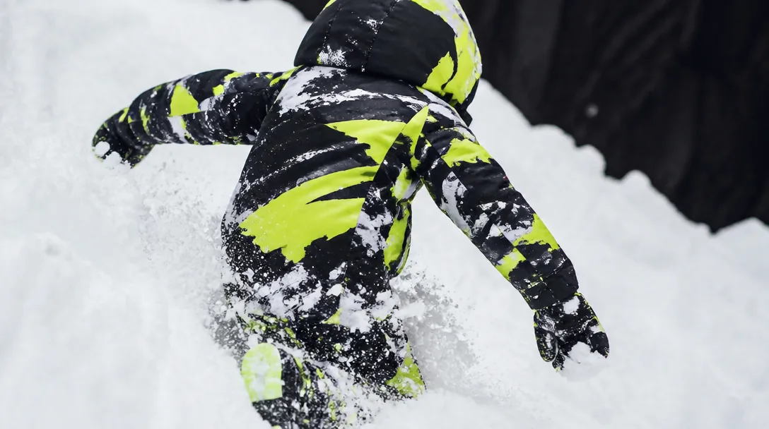 Barn i vinteroverall leker i djup snö, editorial streetwear-stil med lime-accent